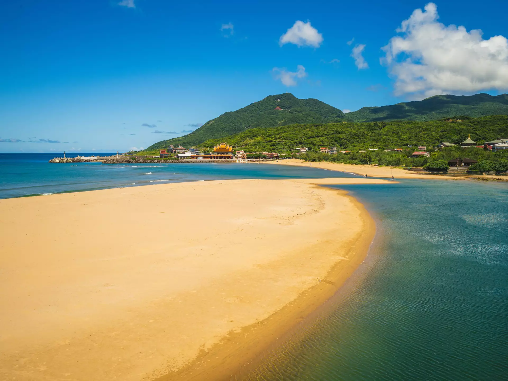 A beach with an arc of golden sand lapped by waves on both sides.