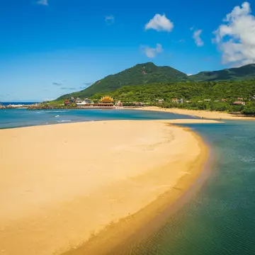 A beach with an arc of golden sand lapped by waves on both sides.