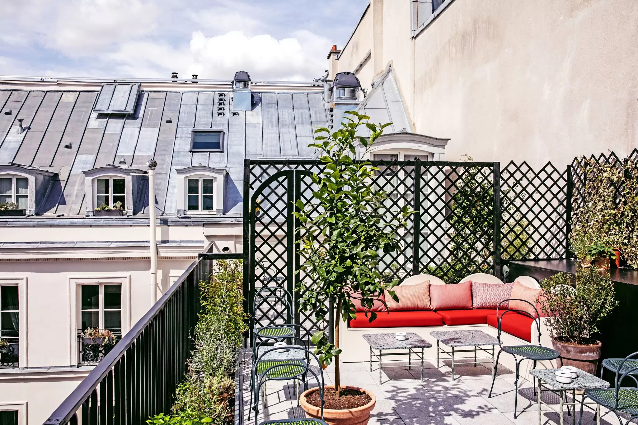 A red couch on a roof terrace surrounded by plants, with views of the grand buildings nearby: Grands Boulevards Experimental, Paris, France. 