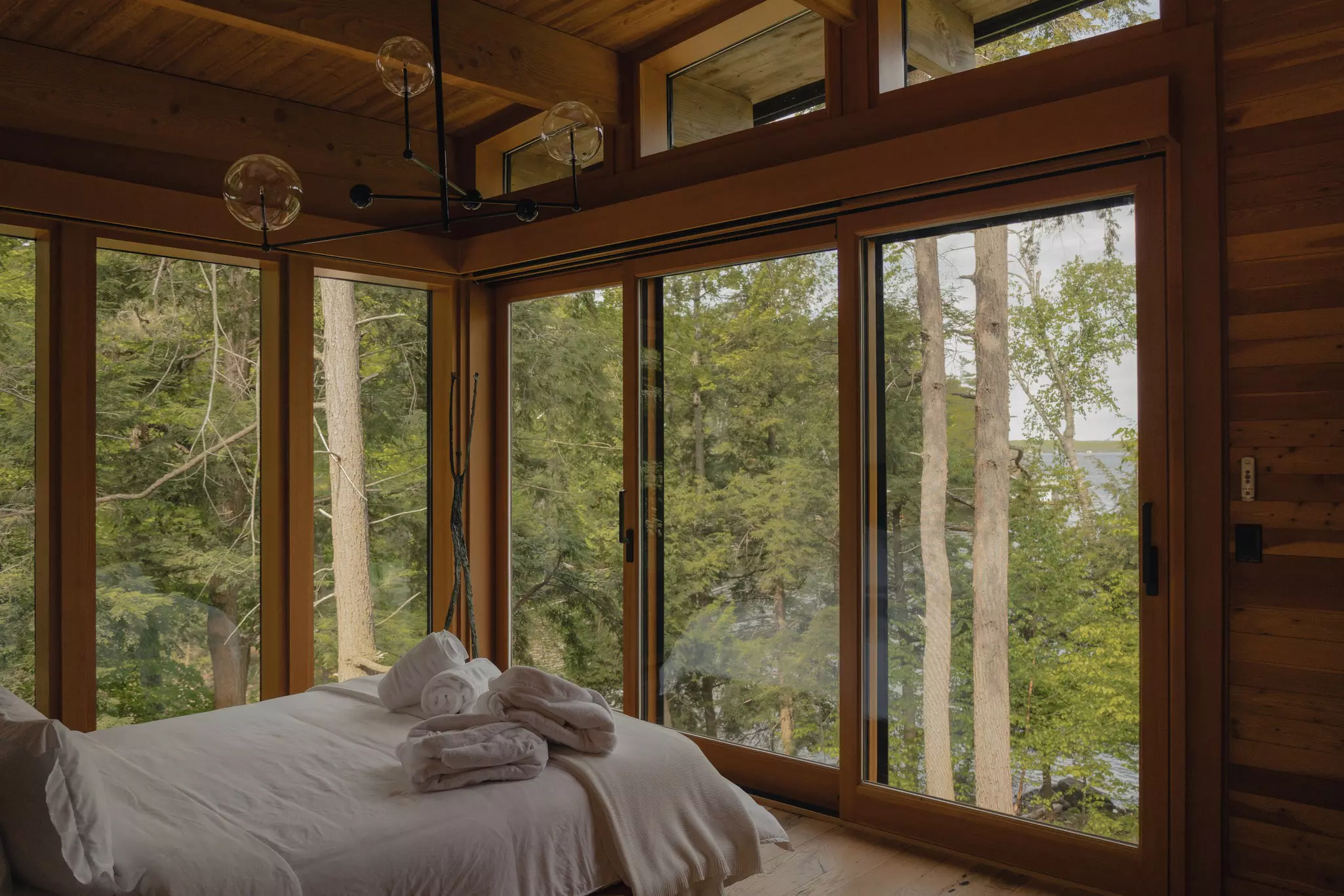 A bed in a room with windows covering all of the walls, with a view of trees.