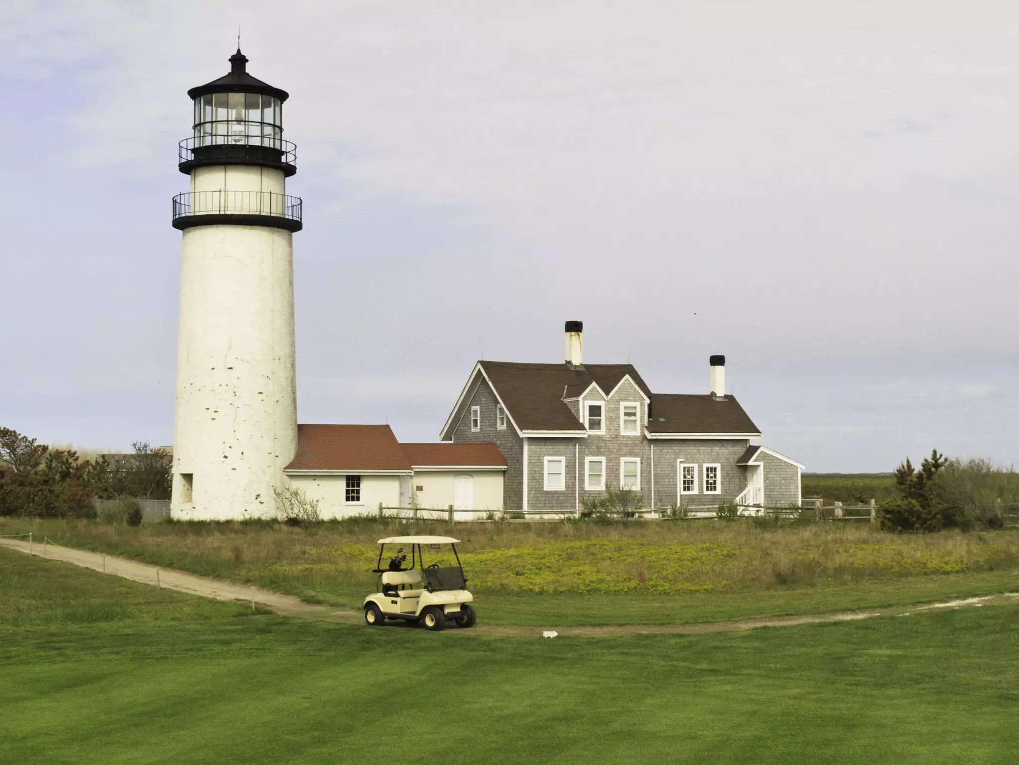 A golf cart on a path on a golf course passes a large white lighthouse.