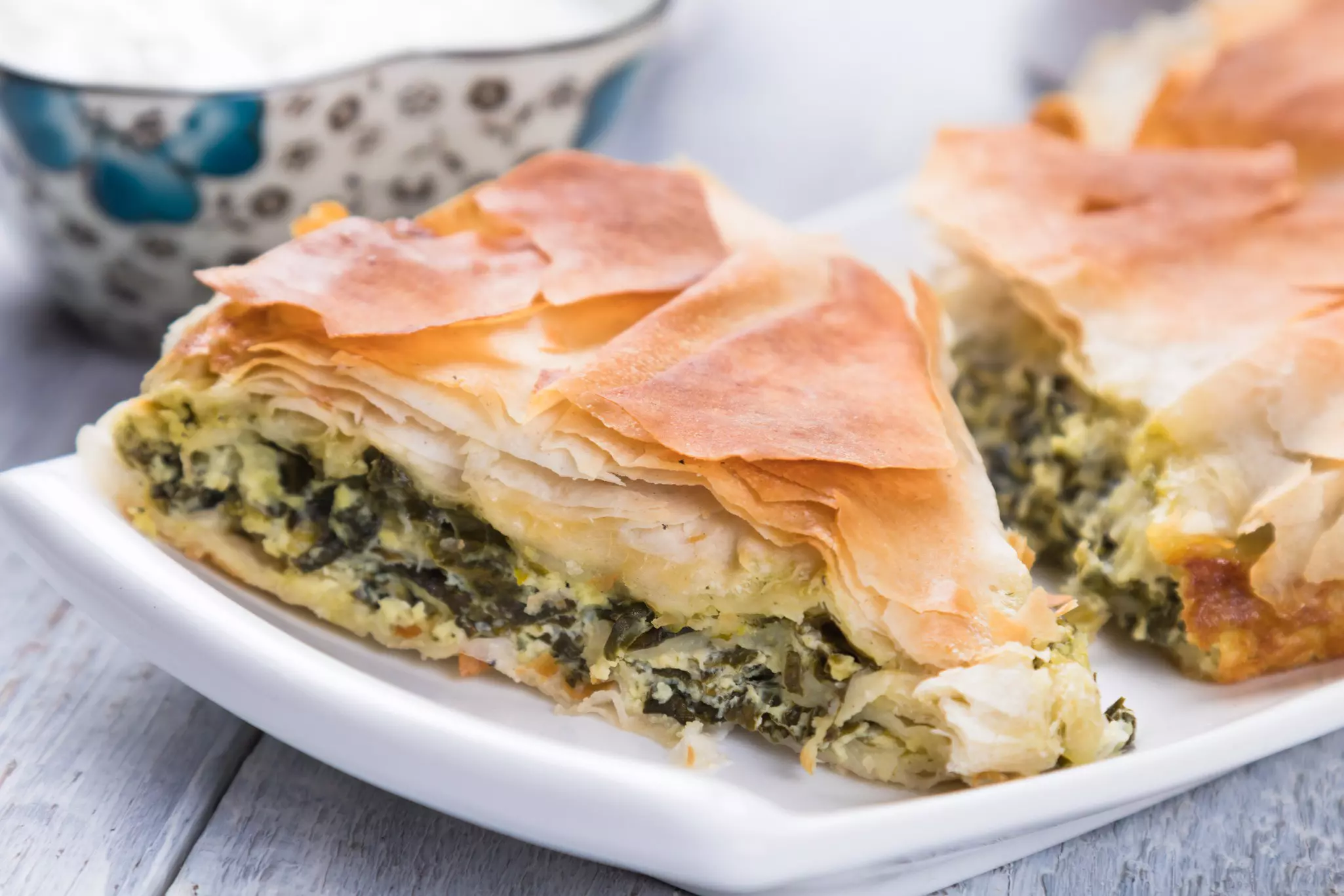 A piece of spanakopita, a greek phyllo pastry pie with spinach and feta cheese filling.
