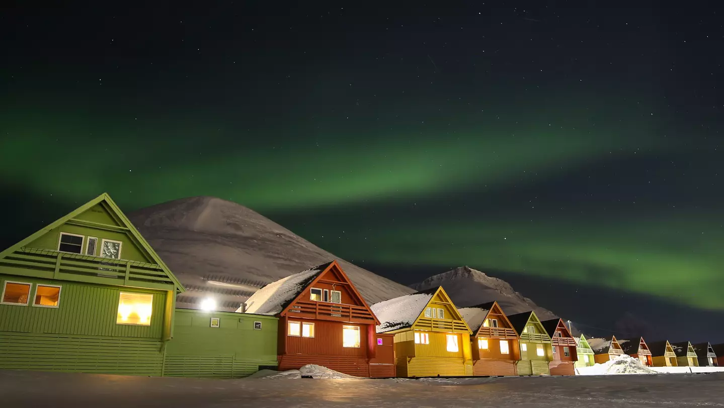 A row of colorful houses in Longyearbyen with a mountain in the background under the northern lights.