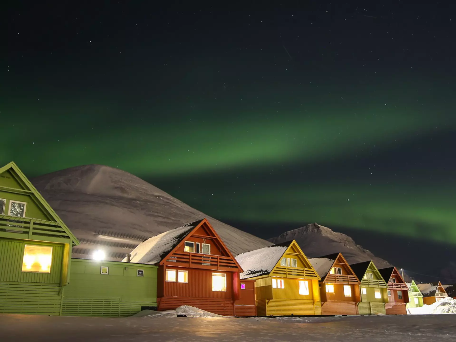 A row of colorful houses in Longyearbyen with a mountain in the background under the northern lights.