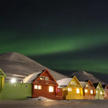 A row of colorful houses in Longyearbyen with a mountain in the background under the northern lights.