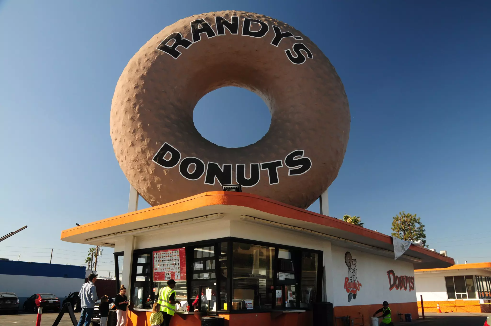 Exterior of a small orang and white shop with a giant doughnut on top that says "Randy's Donuts"
