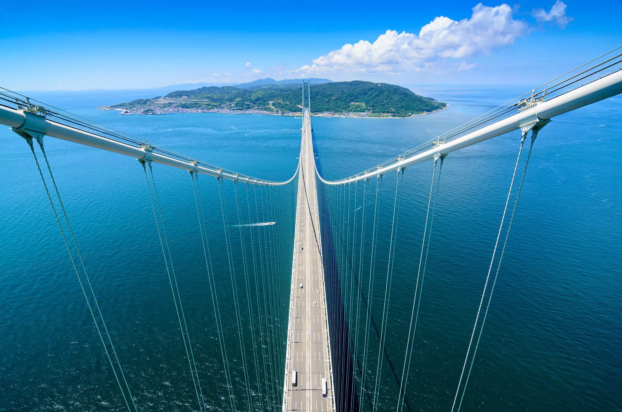 Vehicles drive along a long suspension bridge leading towards an island.