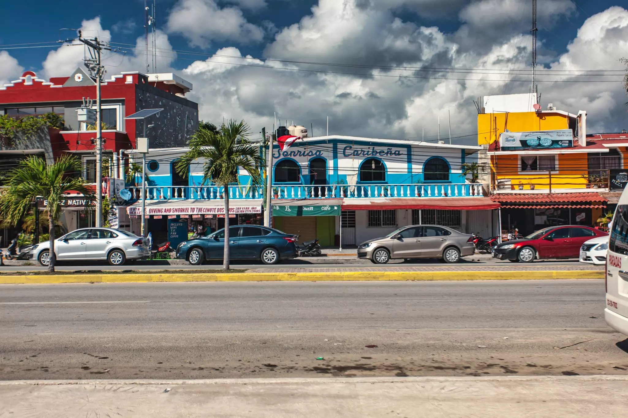 Cars parked at the side of a street in front of buildings painted in bright blue, yellow and red.