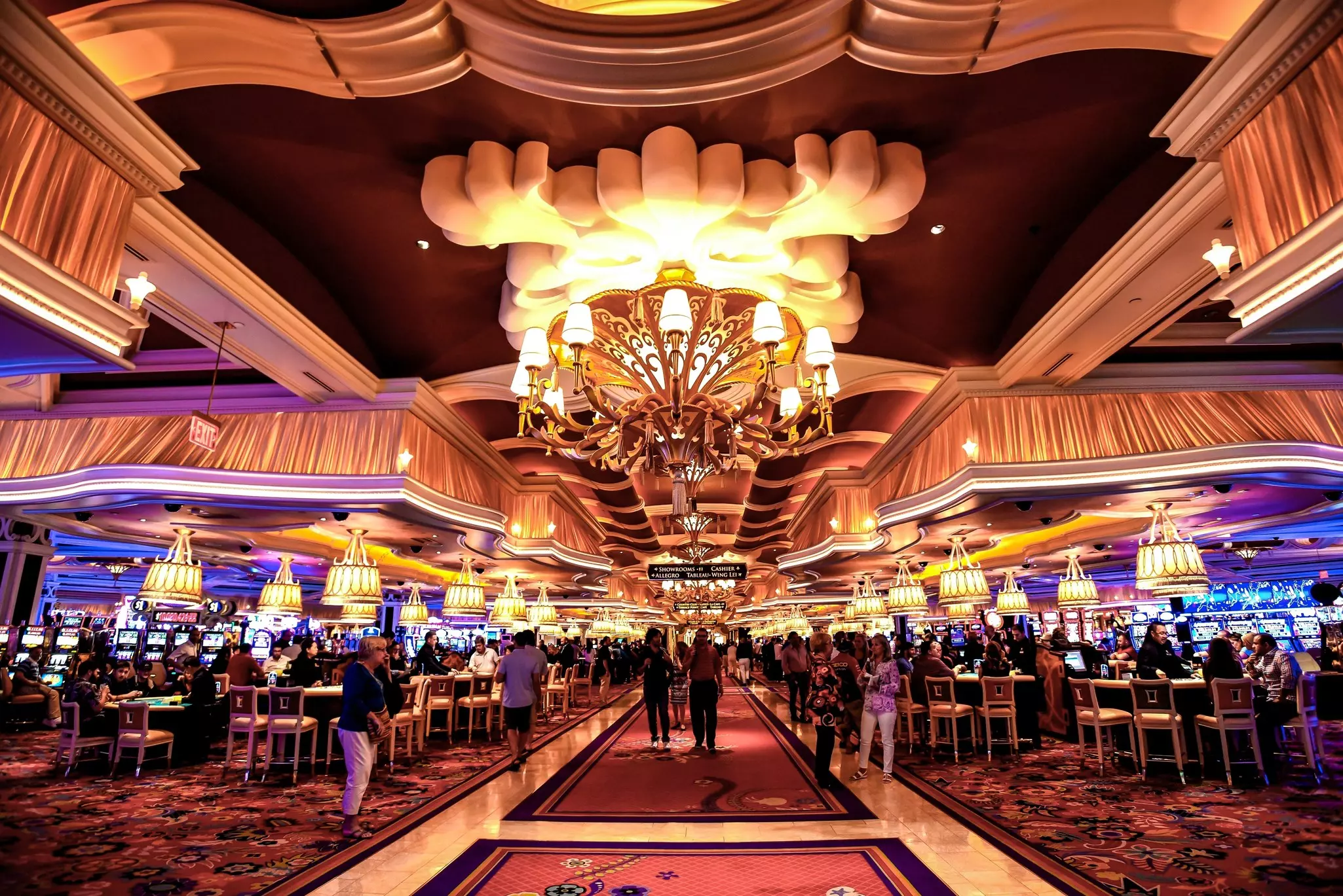 A huge interior space contains electronic gaming stations and casino games. A huge chandelier and fabric valances are installed above the space.