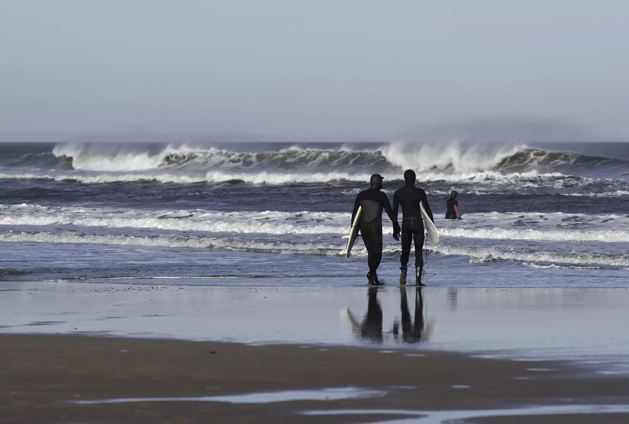 Two surfers walk to the water at Belhaven Bay