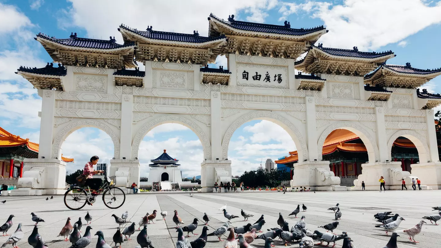 A large white multi-arched gateway with a cyclist passing in front of it