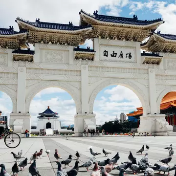 A large white multi-arched gateway with a cyclist passing in front of it