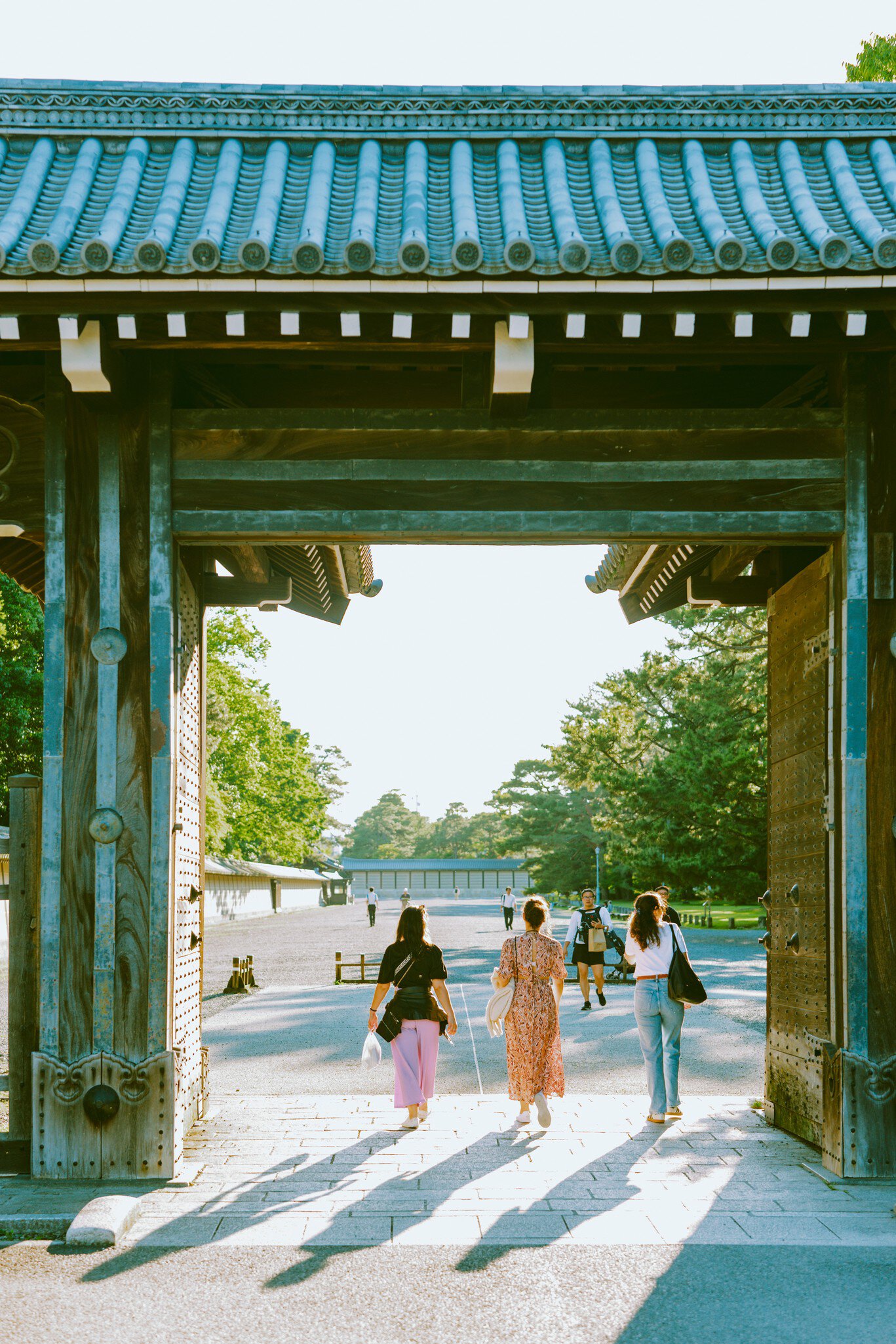 People walk through a gate at a Japanese palace complex into a courtyard.
