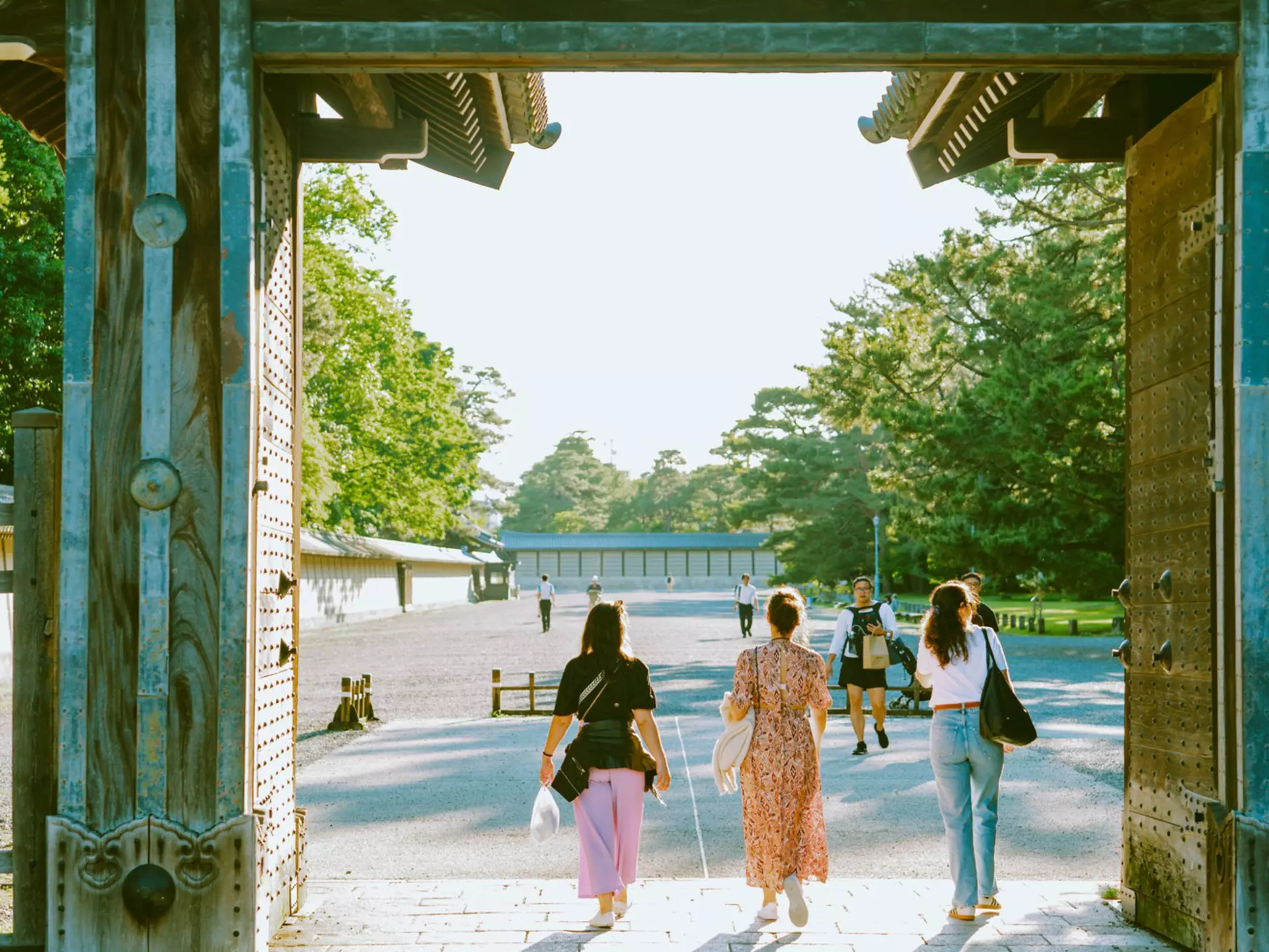 People walk through a gate at a Japanese palace complex into a courtyard.