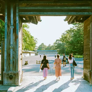 People walk through a gate at a Japanese palace complex into a courtyard.