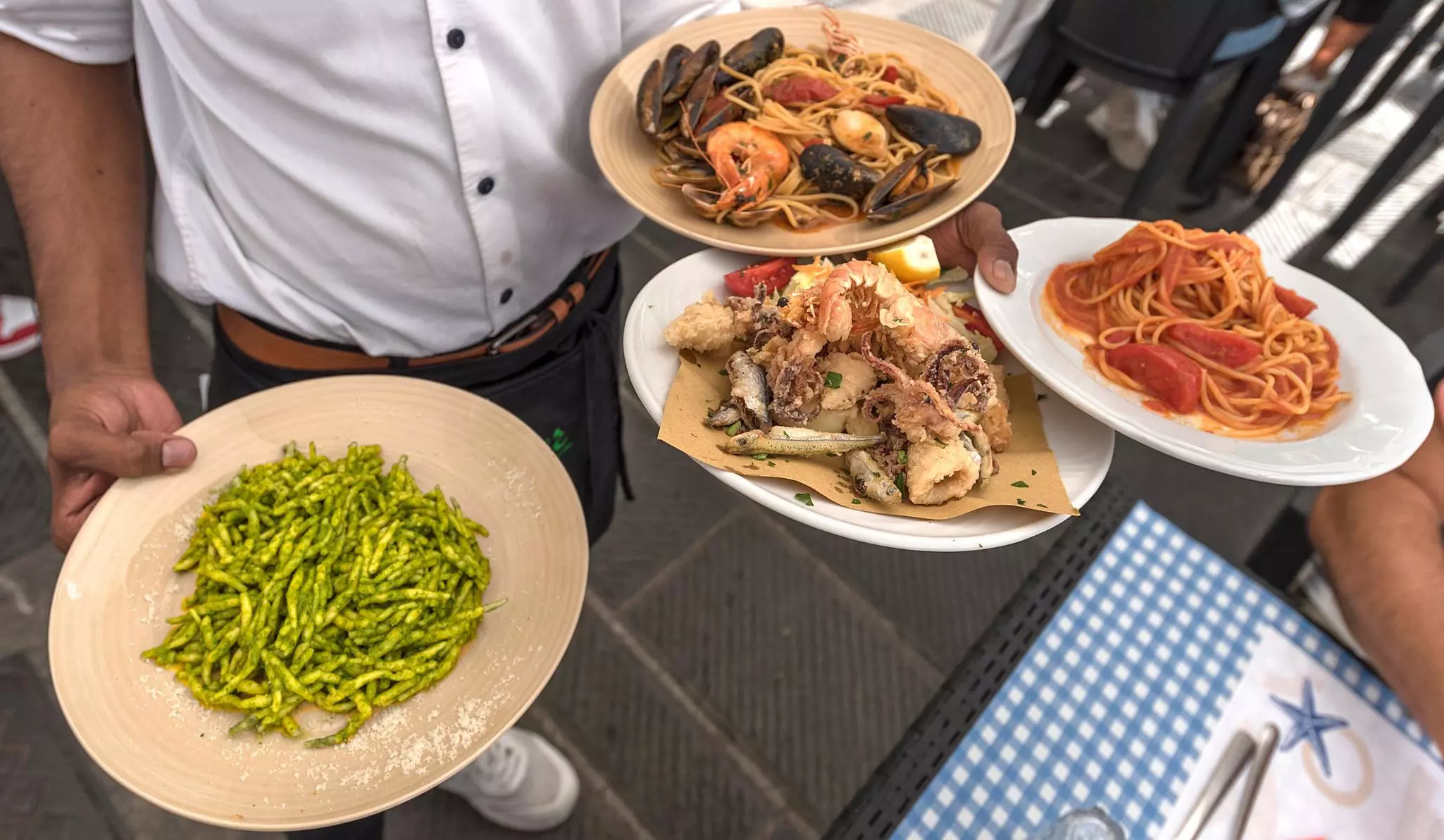 A waiter holds several pasta dishes at a restaurant.