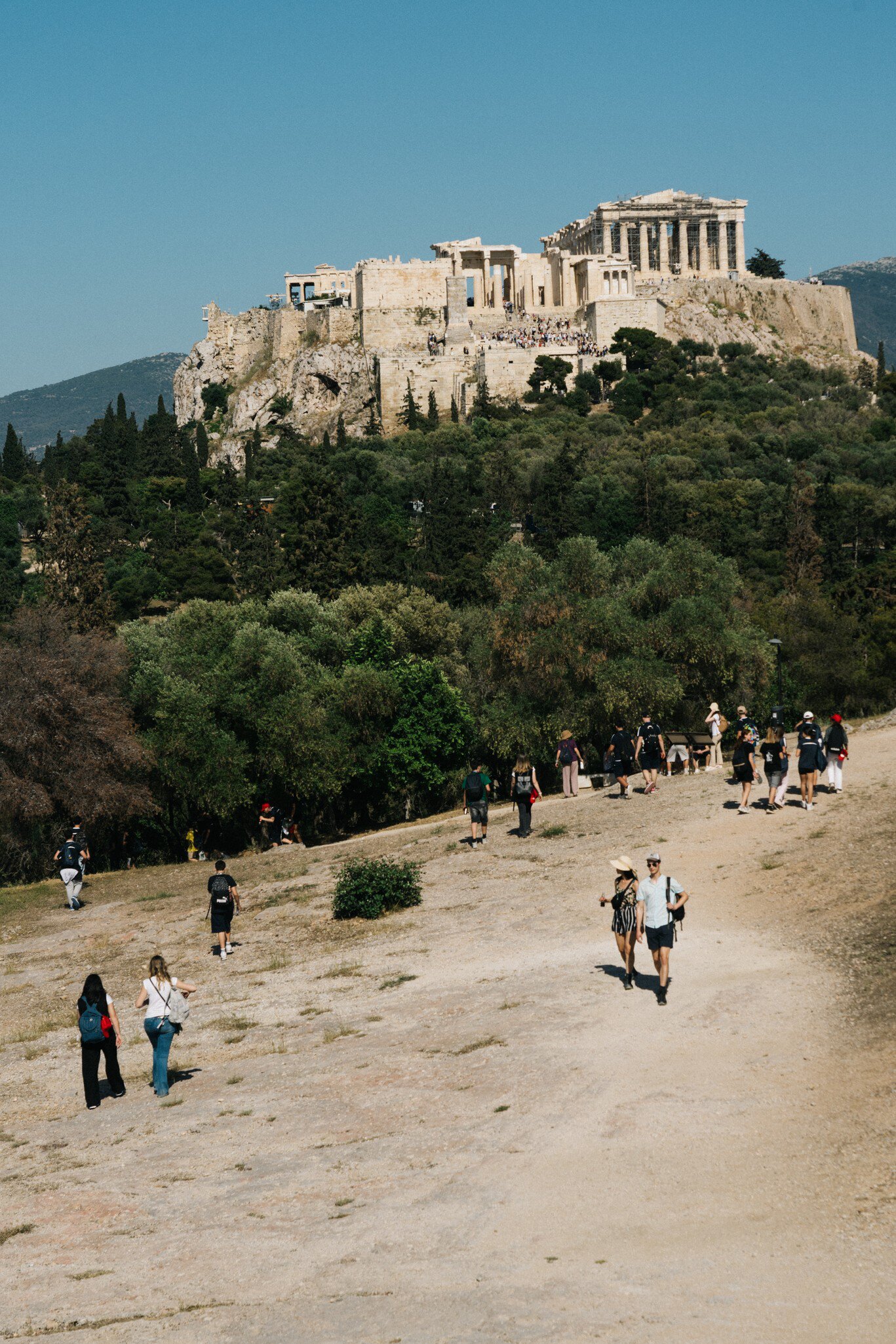 Crowds of tourists walk towards Filopappou Hill on a sunny day in Athens, Greece.