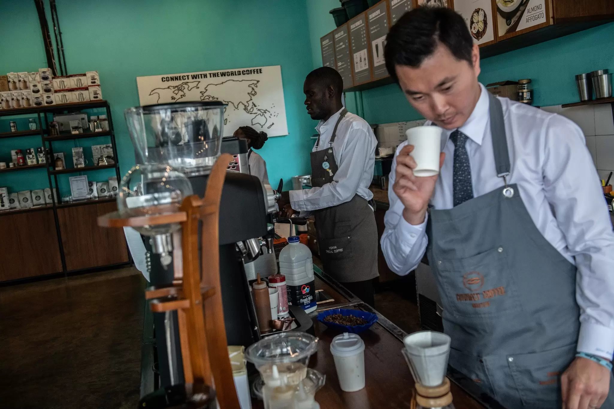 Baristas wearing ties and aprons stand behind a counter making gourmet coffee using speciality tools, Nairobi, Kenya