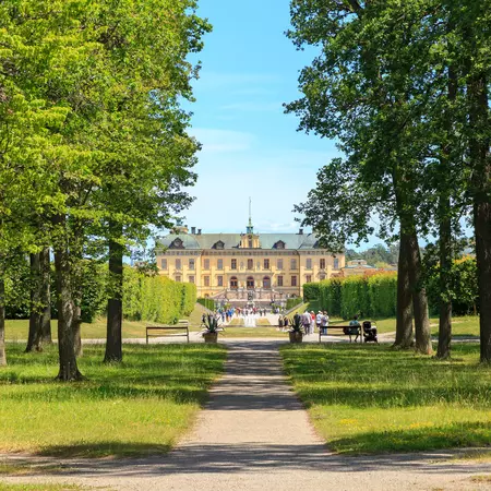 A yellow palace at the end of a path; trees are in the foreground.