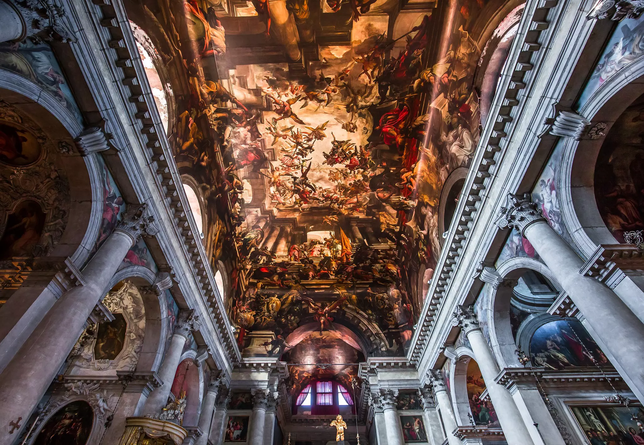 The ceiling of a church covered in ornate art with scenes of angels.