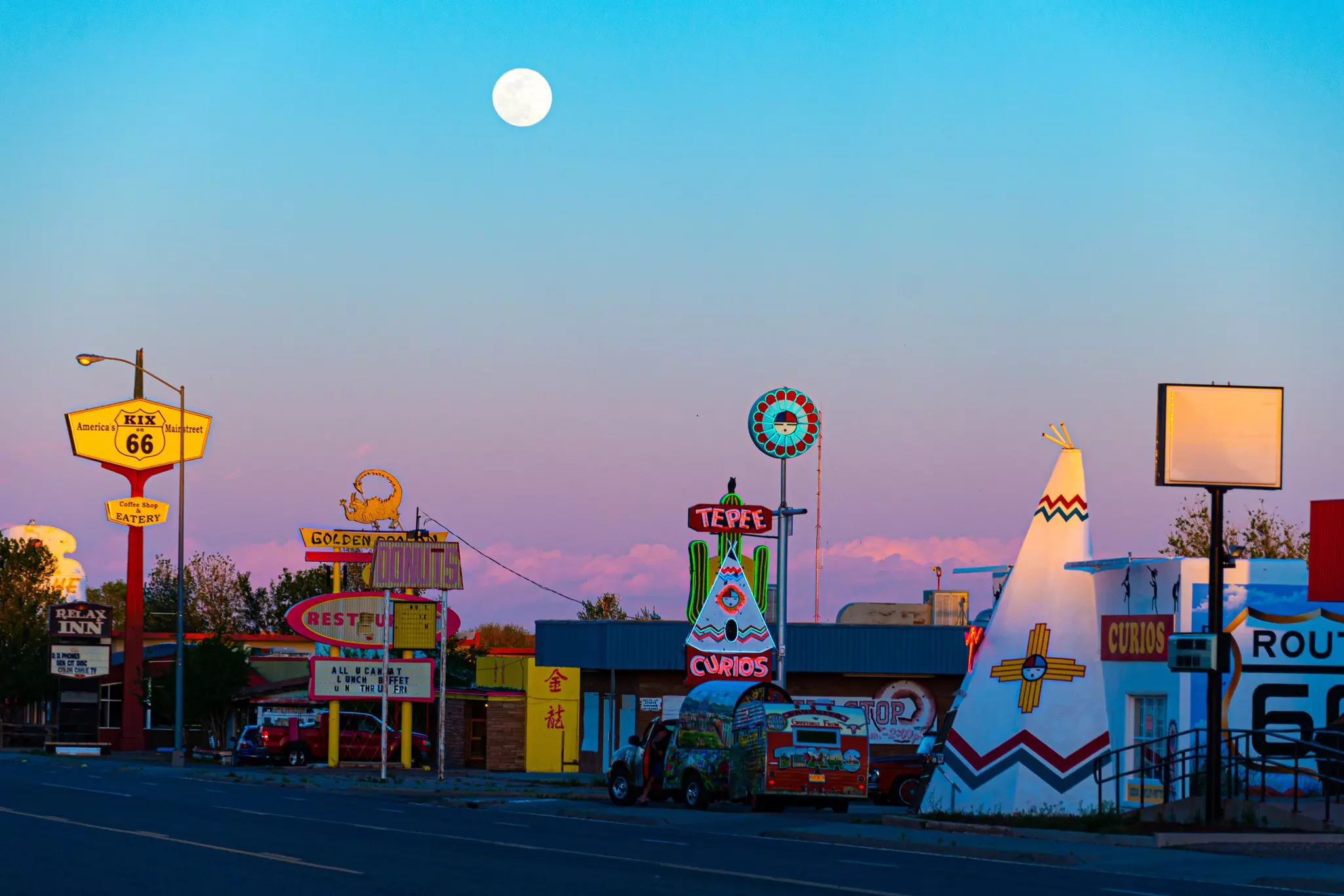 Roadside hotels, restaurants and stores lit up in neon under a full moon.