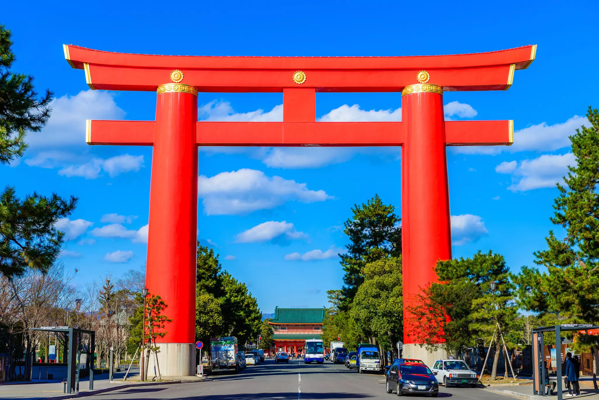 A massive orange gate towers over a city street, serving as the entrance to a temple complex.