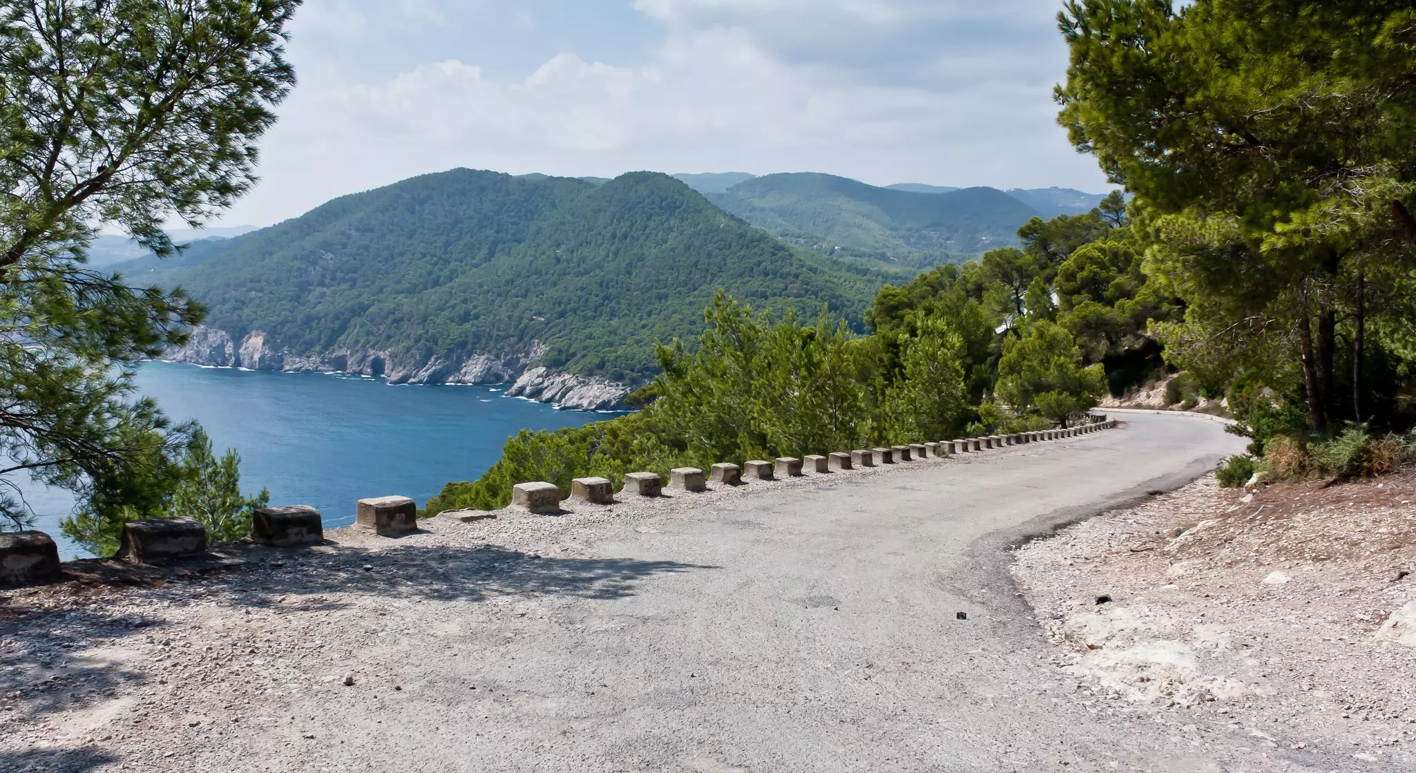 A winding road along a cliff overlooking a beach and the sea on an island.
