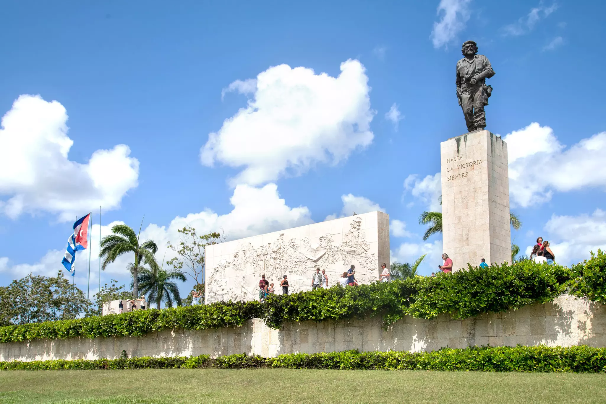 The bronze statue of a man stands on a plinth. Nearby a relief sculpture shows a troop of people.