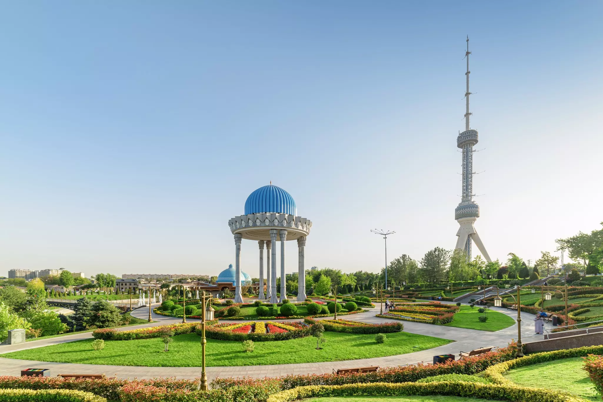 A domed structure in a landscaped garden overlooked by a tall TV tower in Tashkent, Uzbekistan.