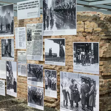 Visitors reading placards beside an excavated cellar wall under a glass canopy
