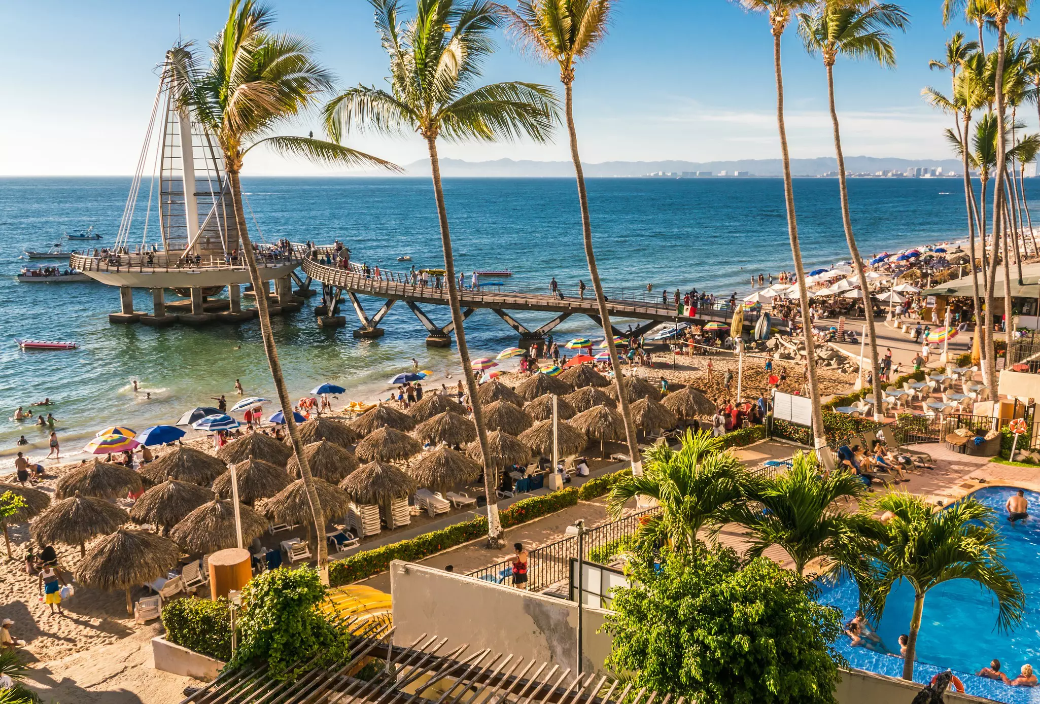 Tourists enjoy the beach at Puerto Vallarta, with people under umbrellas and in the pool.