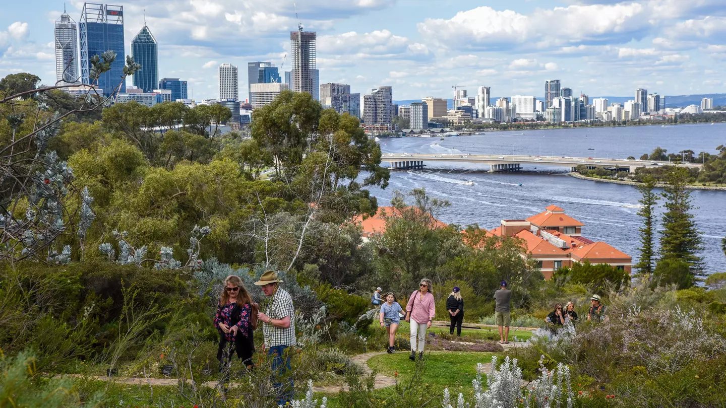 People walk along a path in the lush Kings Park in Perth, with the city in the background.