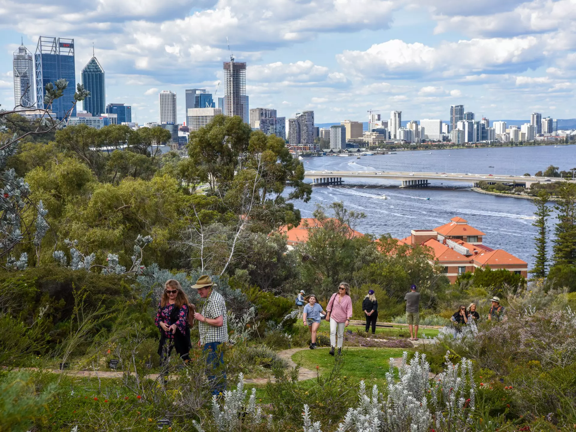 People walk along a path in the lush Kings Park in Perth, with the city in the background.