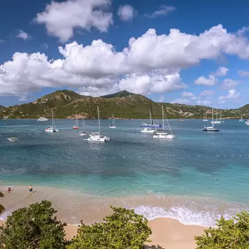 Catamarans moored offshore near a sandy beach being lapped by waves.
