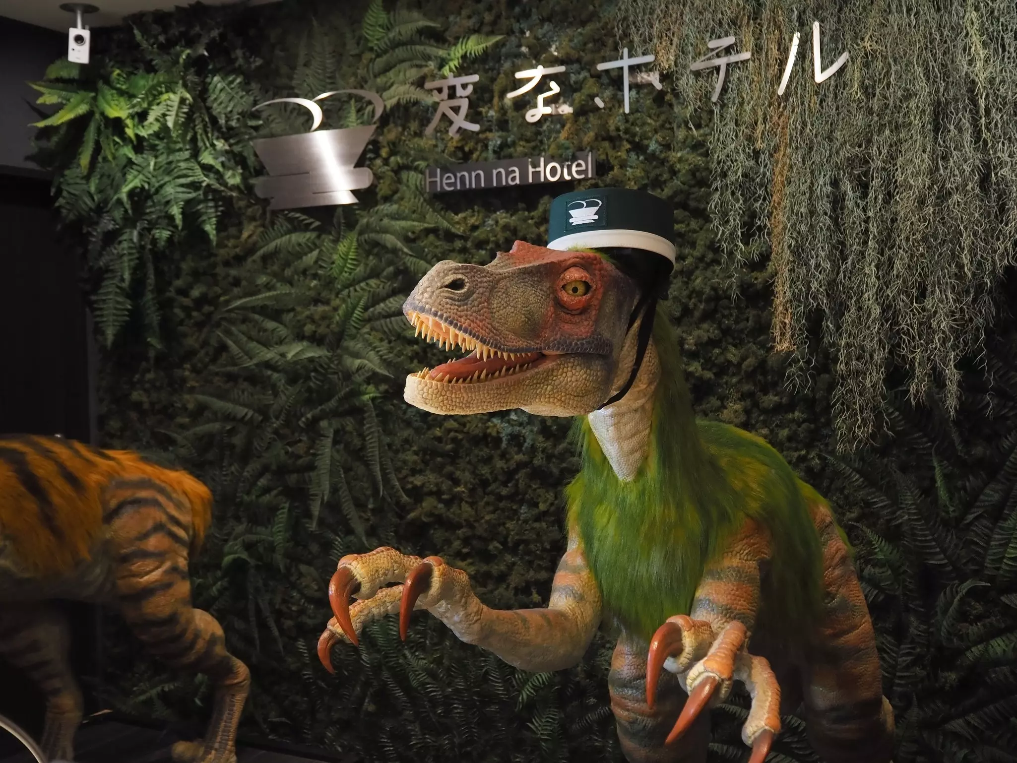 A dinosaur robot by a sign that reads "Henna na Hotel."