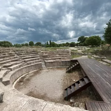 Semicircle of weathered stone tiers around a gravel floor, a boardwalk to the right and storm clouds above