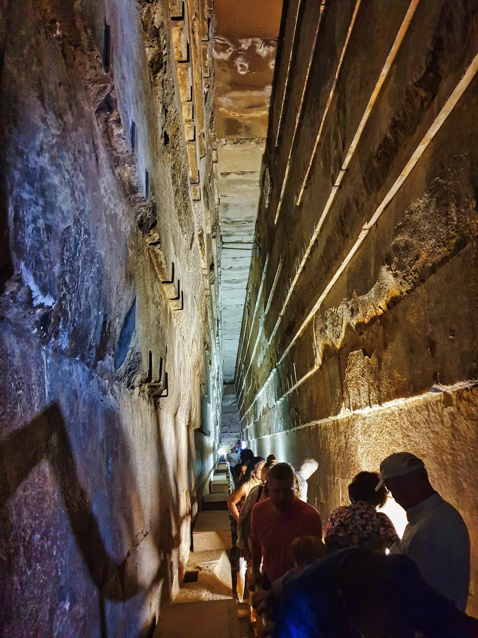 Visitors in a narrow passageway within a stone tomb with slanting walls above them.