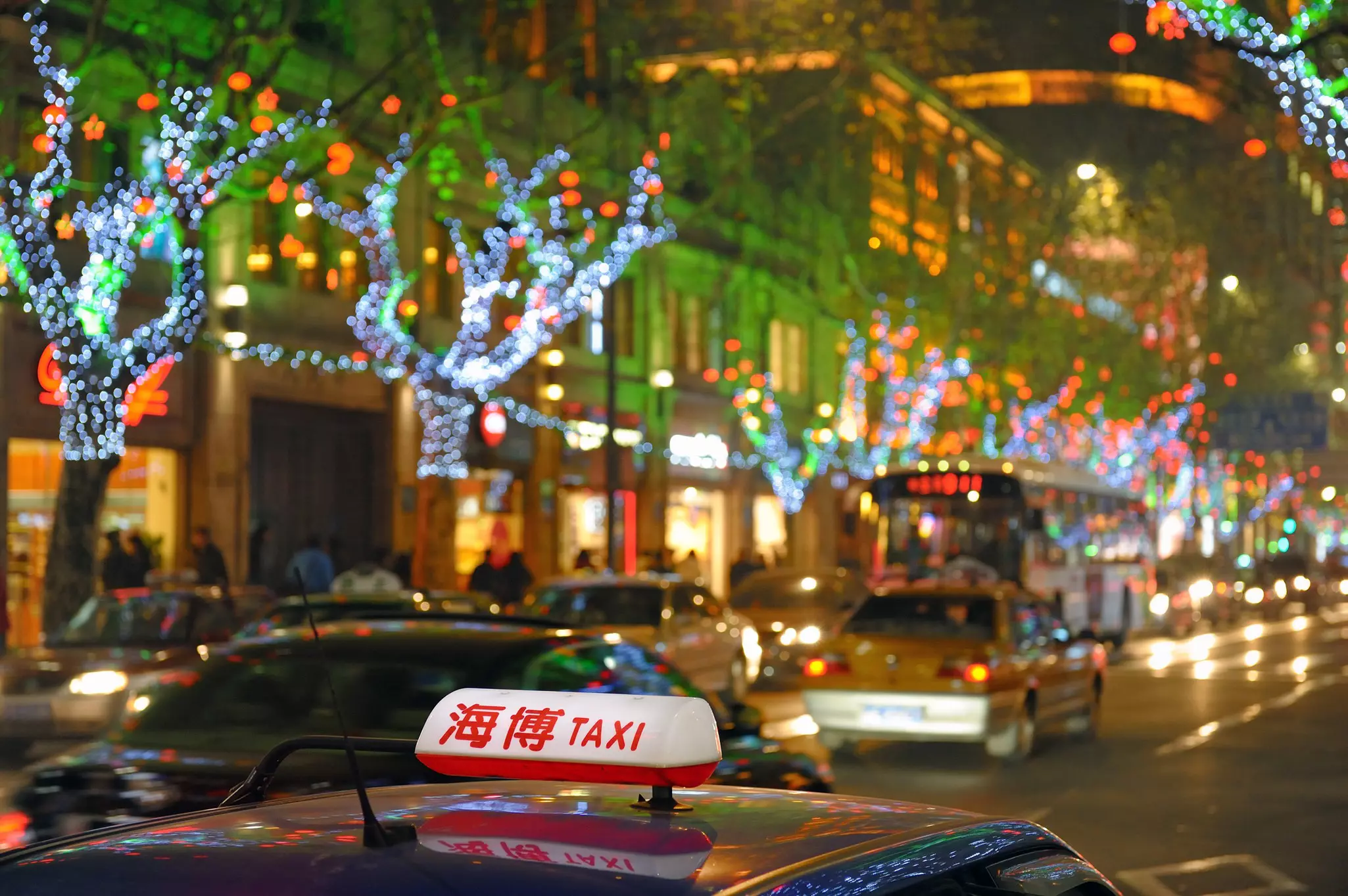 Taxis driving down a road illuminated by colorful lights in Shanghai, China.