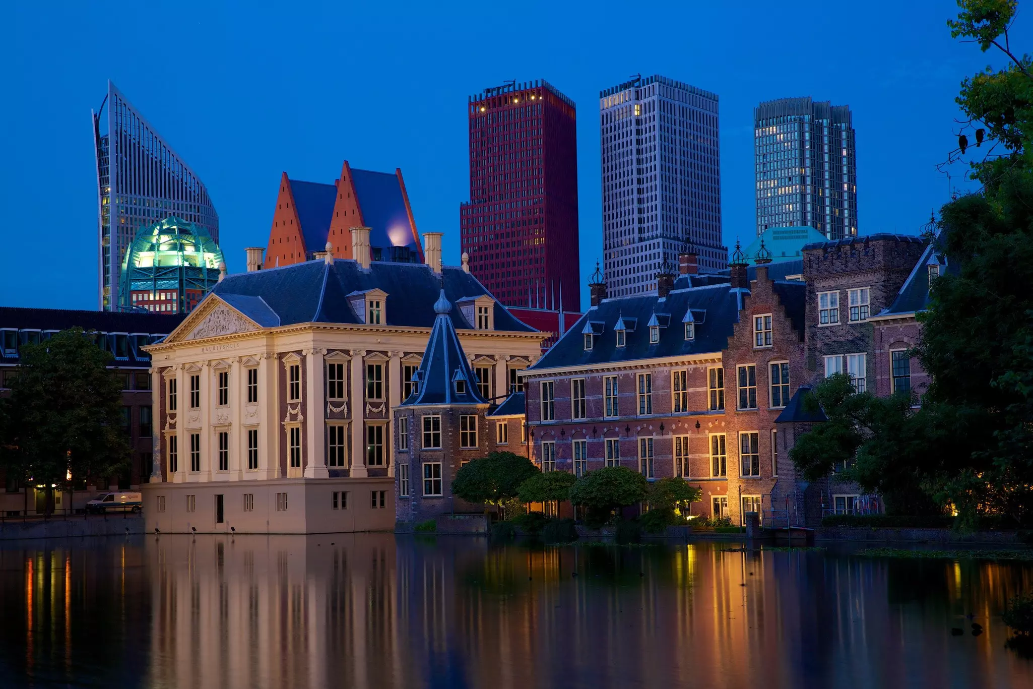 The Peace Palace at dusk with modern city buildings behind it