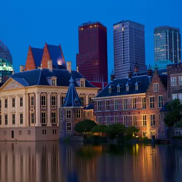 The Peace Palace at dusk with modern city buildings behind it