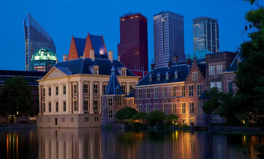 The Peace Palace at dusk with modern city buildings behind it