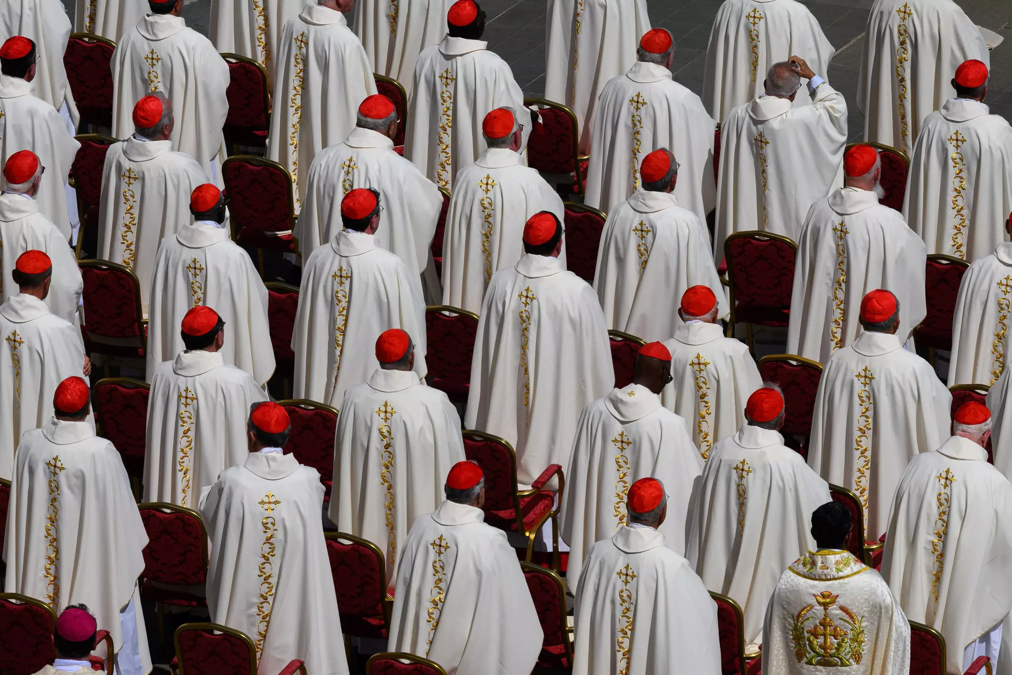 Cardinals dressed in white robes and red caps attend mass.