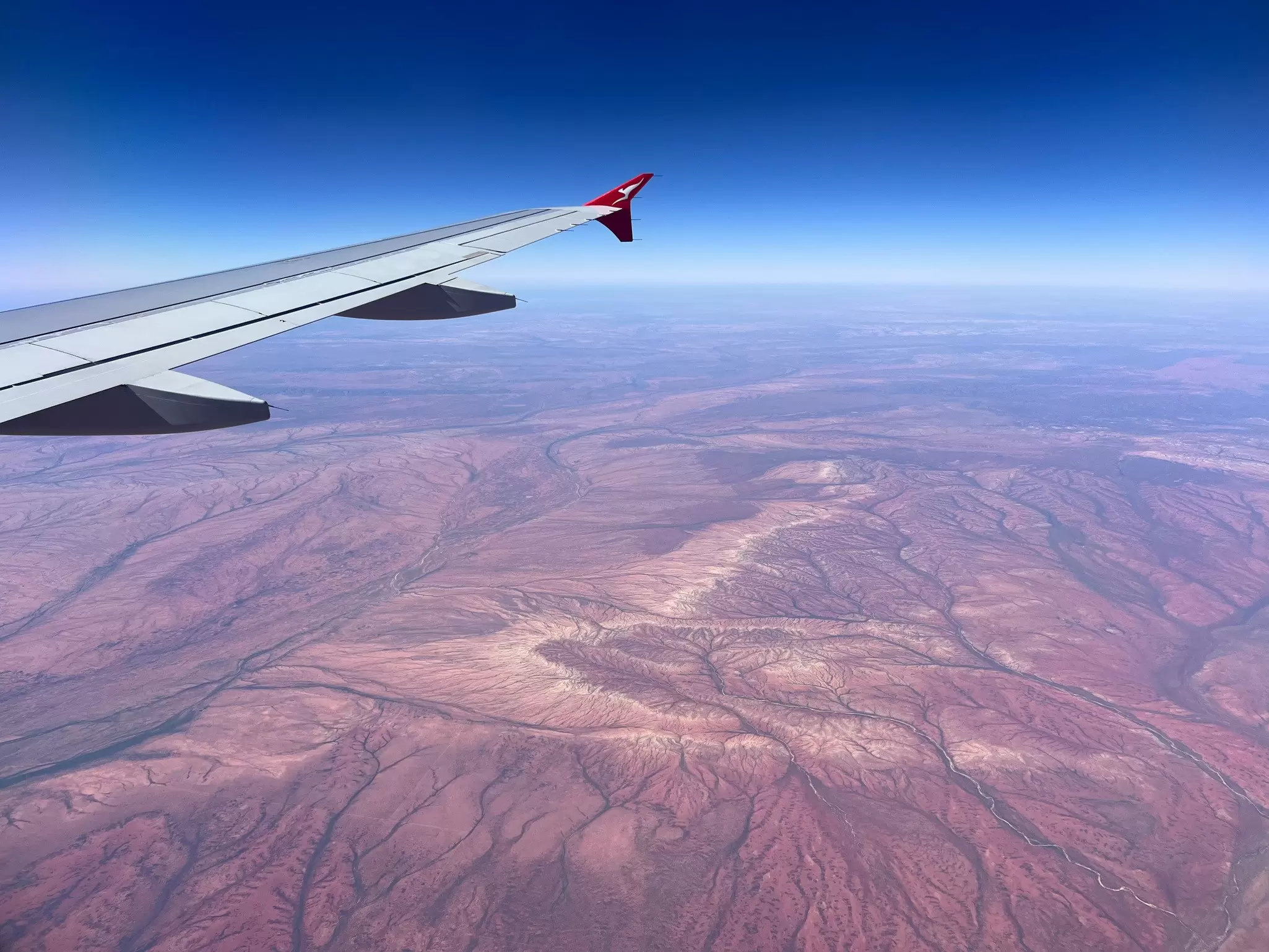 A plane wing overtop of a red, empty desert.