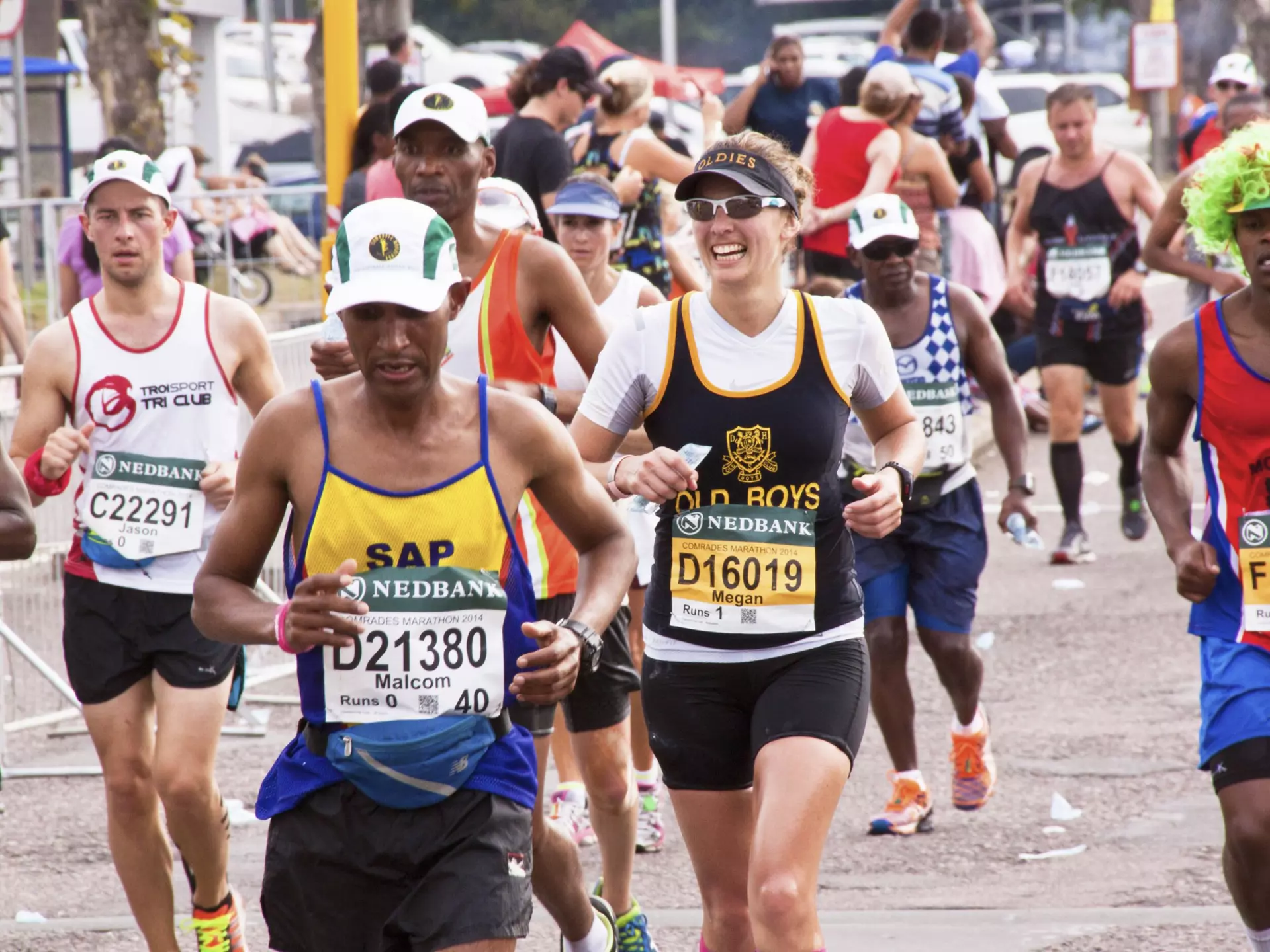 A group of competitors wearing numbered bibs run along a stretch of road in an ultra marathon