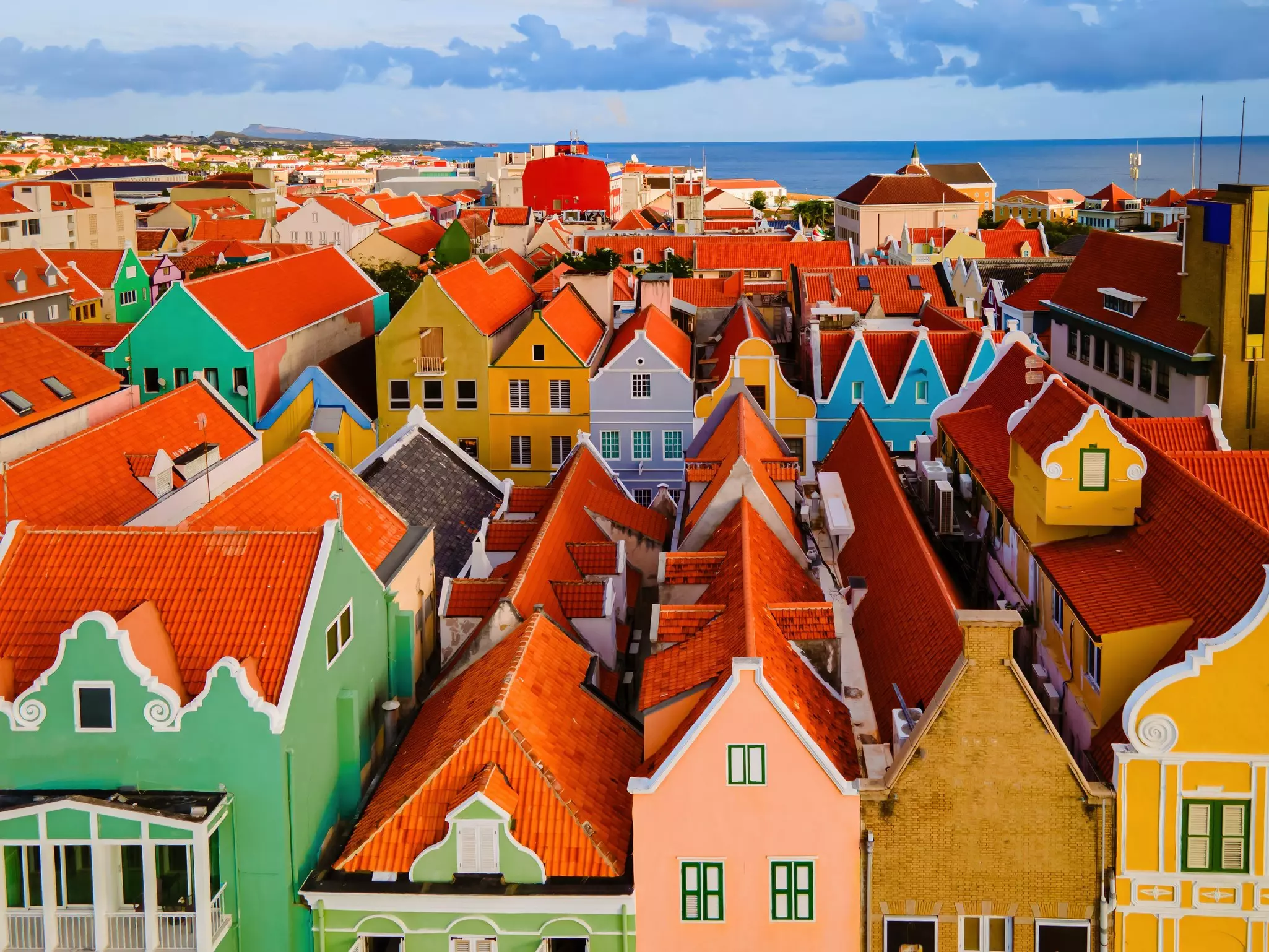 An overhead view of the red-tiled roofs on historic buildings in a tropical city. The buildings’ facades are painted in bright colors.