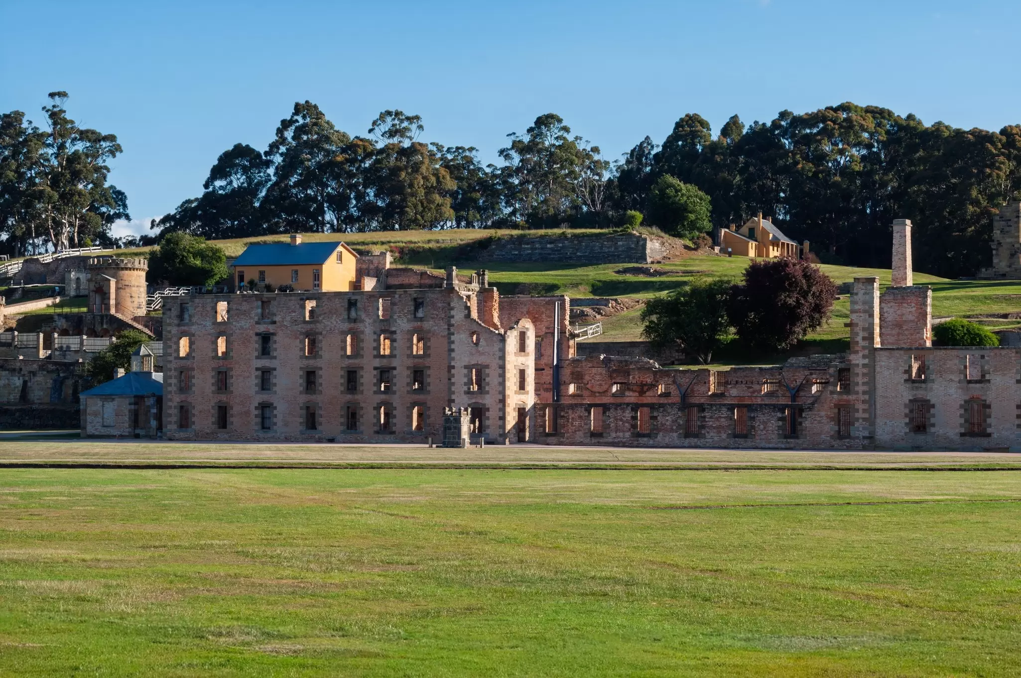View of sandstone prison buildings, lawns and the surrounding hills at Port Arthur Historic Site in Tasmania, Australia.