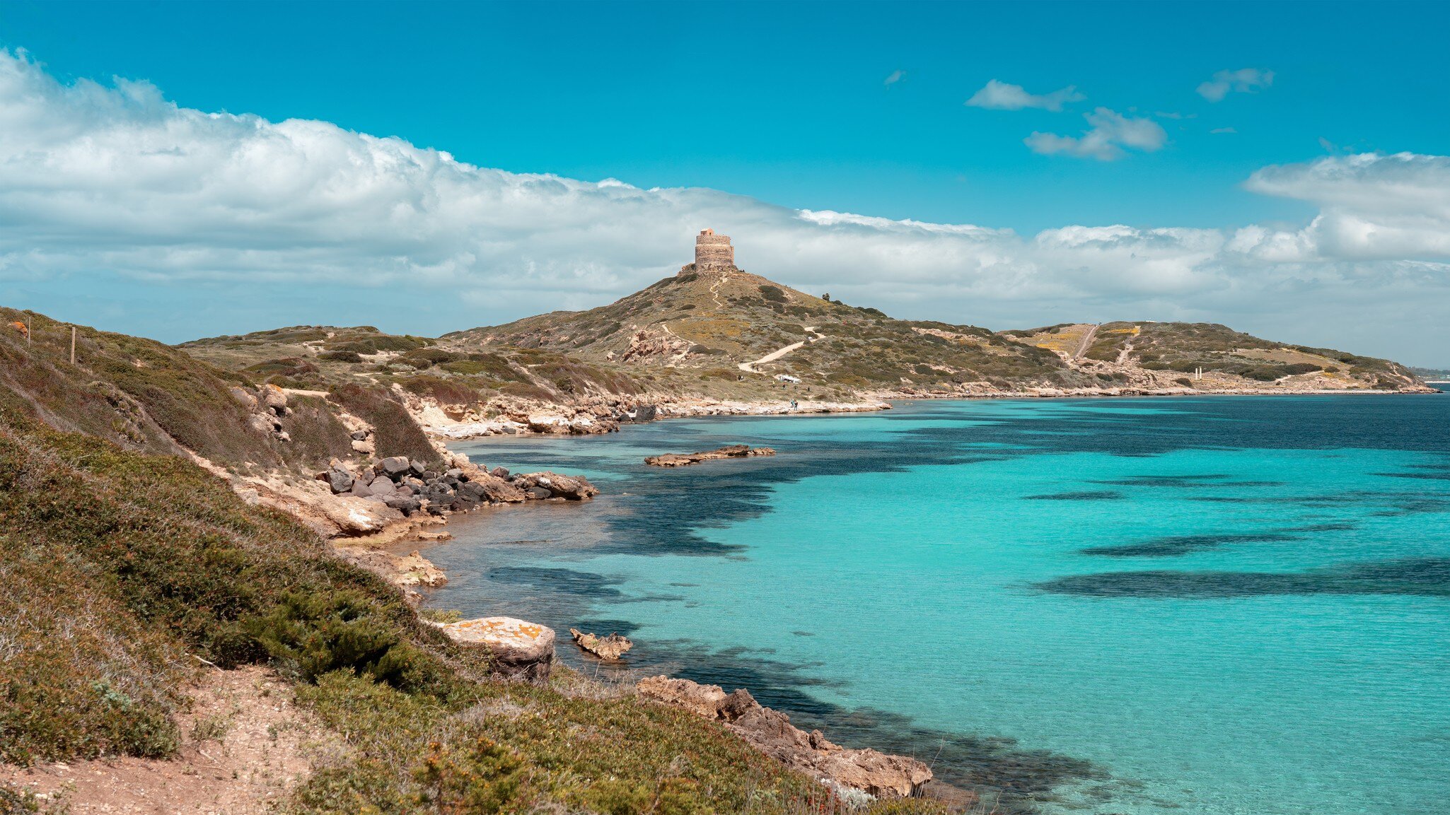 Landscape of Capo San Marco, Sinis peninsula, with the tower of San Giovanni and the ruins of Tharros in the background, contrasting with the emerald water.