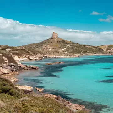 Landscape of Capo San Marco, Sinis peninsula, with the tower of San Giovanni and the ruins of Tharros in the background, contrasting with the emerald water.