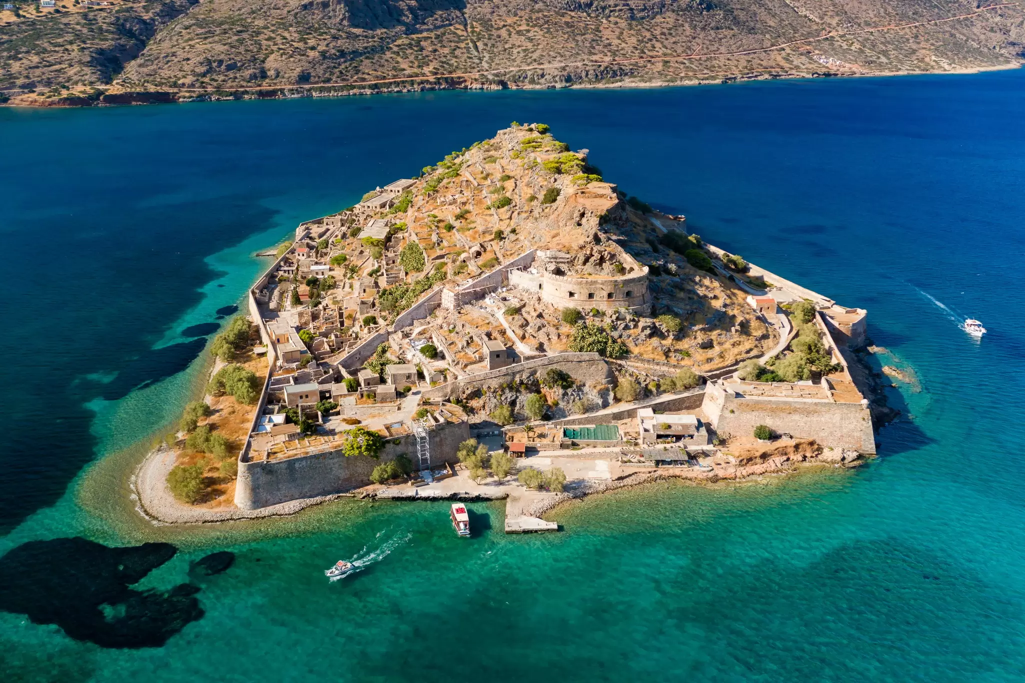 Aerial drone view of the Venetian fortress island as boats circle the harbor on a sunny day.