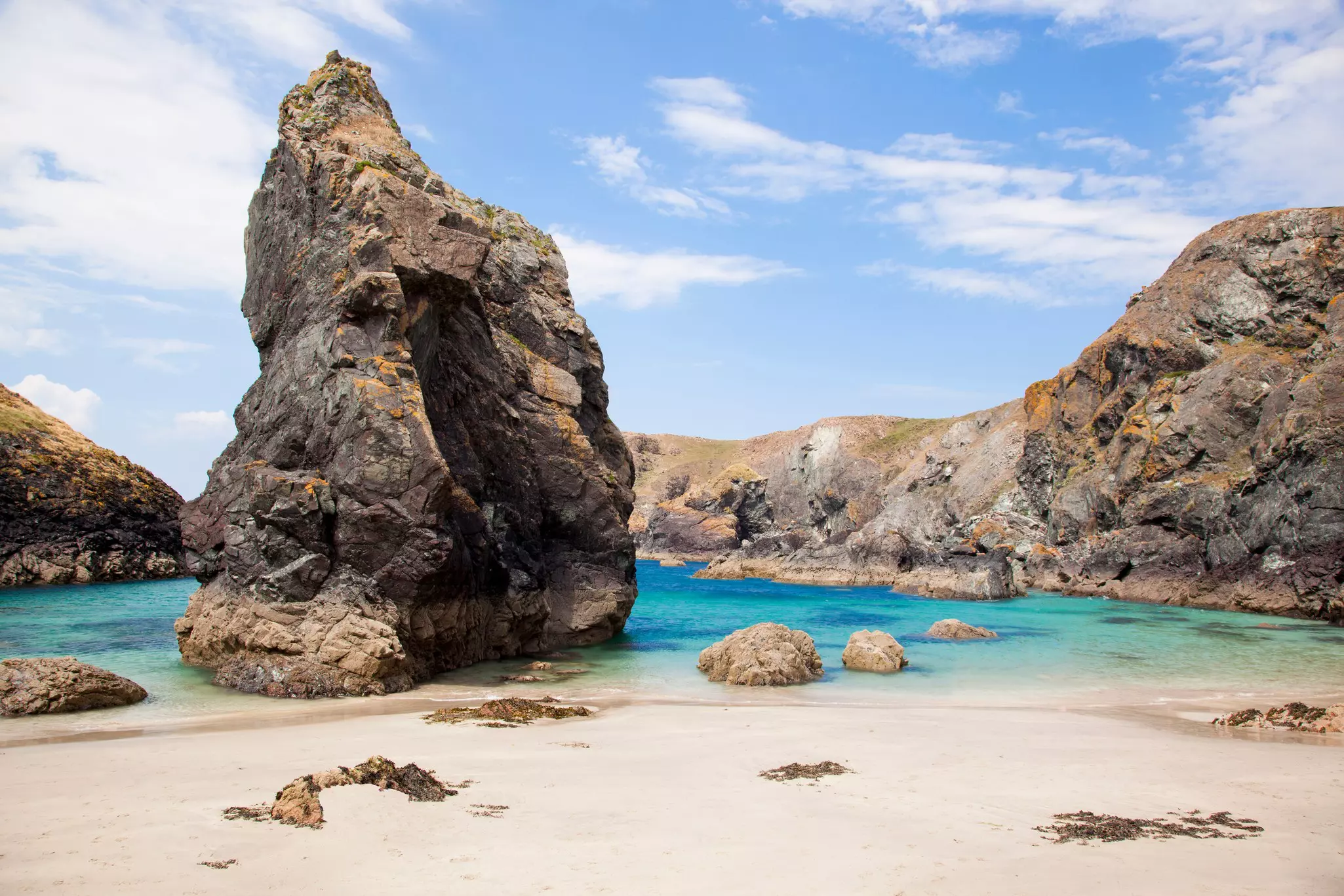 A large pointed rock standing tall in a sheltered sandy cove.